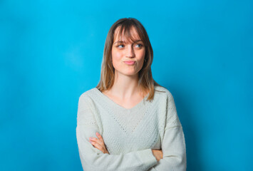 Fototapeta premium Fun portrait of a charming young woman. The background is blue. She is looking to her side and has piercing blue-eyes. She is smiling, she looks playful and happy.