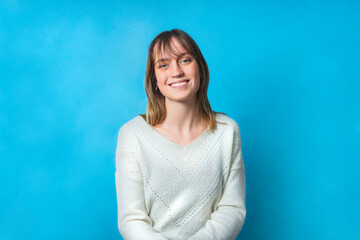 Beauty portrait of a charming young woman. The background is blue. She is looking straight at the camera and has piercing blue-eyes. She is smiling, she looks joyful and happy.