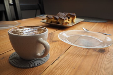 Filiżanka z kawą, szklany talerz i ciasto na drewnianym stole