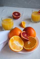 Sweet and juicy blood oranges and oranges, whole and cut on a white plate and glasses of fresh orange juice. Fresh orange juice with Sliced oranges.