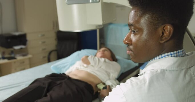 Lithotripsy for kidney and ureteral stones in modern center. Professional African man doctor, using ultrasound scan to determine the stone position before the lithotripsy for his female patient