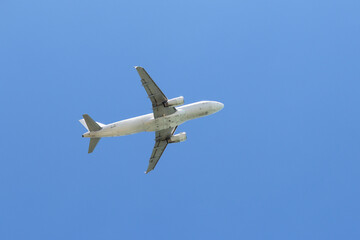 Airplane flying in the clear blue sky, bottom view. Commercial plane taking off and gaining altitude