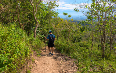 Obraz premium Trekker with backpack on the trail. Trekker on trail on natural landscape background. Summer countryside hiking trail view with male tourist. Man in treking or hiking outfit. Active lifestyle.
