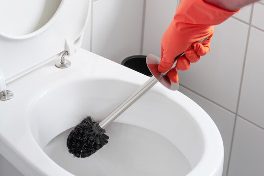 person wearing rubber gloves cleaning toilet bowl with toilet brush