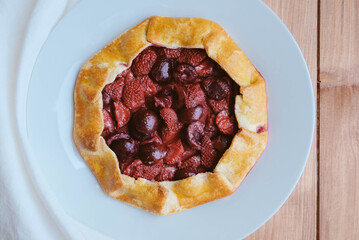 Delicious freshly baked vegan strawberry and cherry galette on wooden rustic background, top view. Sweet food, summer dessert.