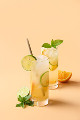 Cold and refreshing lemonade or cocktail with orange and lime slice on beige vertical background. Summer drink.