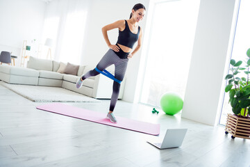 Full size photo of happy good mood beautiful girl exercising with rubber expander on fit mat watch video in laptop at home