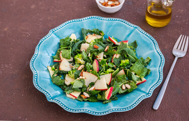 Healthy salad with kale, apple and almonds in a blue plate on a brown concrete background. Kale recipes.
