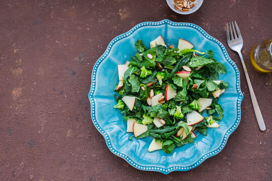 Healthy salad with kale, apple and almonds in a blue plate on a brown concrete background. Kale recipes.