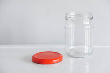 Empty glass jar with red cover on white table background. Copy, empty space for text