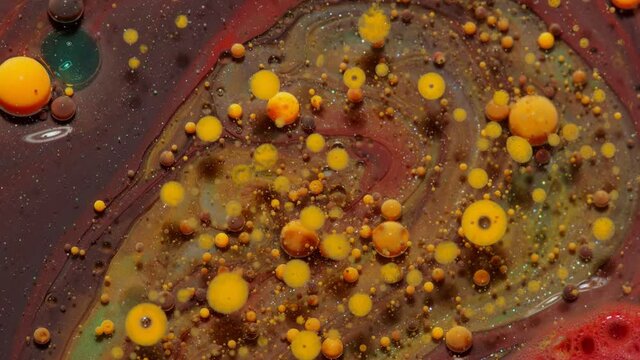 Top view movement of bright oil bubbles in slow motion. Multicolored surface background. Fantastic universe structure of colorful moving orange bubbles. Artistic image of ink drops floating on water