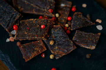 Beef jerky on black stone surface. Dried meat.