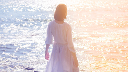 Young woman in white dress enjoys sea. Back view.