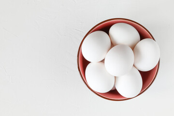 White hen eggs in a nice bowl on a white table - top view and close up