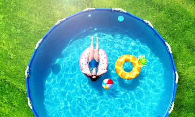 Foto auf Acrylglas Aerial. Girl resting in a metal frame pool with inflatable toys. Summer leisure and fun concept. Frame pool stand on a green grass lawn. Top view from drone. © Dmytro