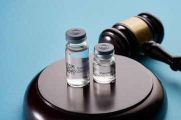  Law and vaccination concept. bottle of covid-19 vaccine, gavel and syringe on blue background.