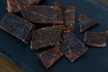 Beef jerky on black stone surface. Dried meat.