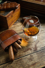 short cigars on a wooden table inside a leather cigar case and a glass of cognac