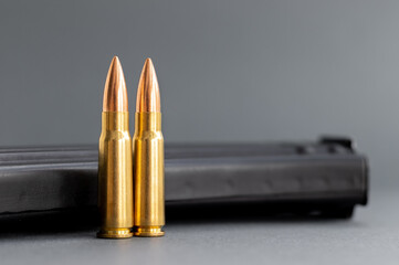 Two bullets against Kalashnikov assault rifle clip, magazine on blurred gray background. Cartridges...