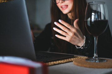 Young millennial woman having video call on laptop computer and drinking wine, use technology for communicate with friends or family.