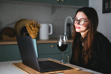 Young millennial woman having video call on laptop computer and drinking wine, use technology for...