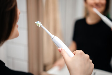 Electric toothbrush in the hands of a woman in the bathroom. Interior mirror and reflection.