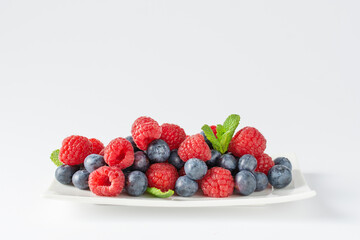Fresh blueberries and raspberries plate on white background.