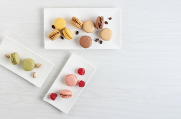 Variety of french macaroons with raspberry, coffee and pistachio on a plate on white wooden table.