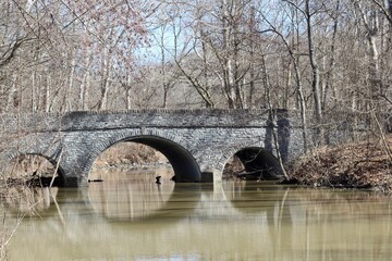 Fototapeta na wymiar The old stone bridge over the creek in the park.