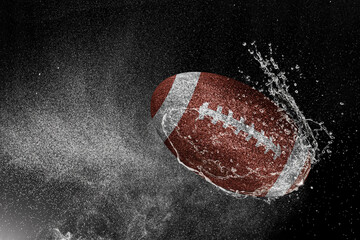 American football ball flying in water drops and splashes isolated on black background