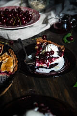 Piece of homemade cherry and custard pie with vanilla ice cream on glass plates on dark wooden table.