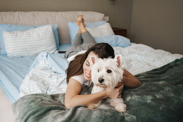 Happy white woman stroking her dog while lying on bed at home