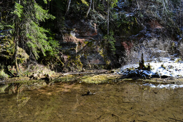 sandstone cliffs on the bank of a forest river with a perfect reflection in the water and green conifers on the bank.