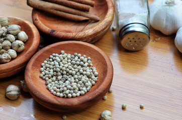 pepper, cardamom, and cinnamon in a wooden bowl on a wooden tray plus garlic and salt. close up with selective focus