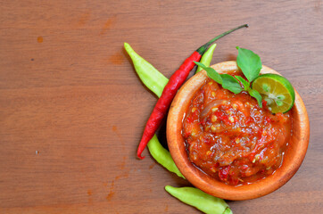 chilli paste (sambal terasi) in a wooden bowl with garnished basil leaves and lime wedges. selective focus