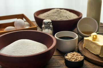 Ingredients on wooden table, flour, eggs, sugar, milk, essences, butter, salt, prepared for recipe