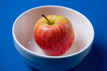 Manzana en bol blanco con fondo celeste