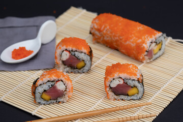 Sushi rolls with salmon avocado tuna and mango in a mat and black background