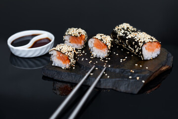 sushi roll with salmon and tuna with sesame and soy sauce y a black stone background