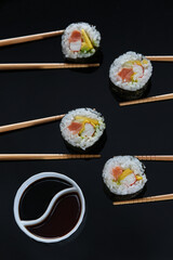 Sushi rolls with salmon avocado tuna and mango in chopsticks soy sauce and a black background