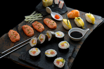 Sushi rolls nigiri, uramaki, hosomaki with salmon  and mango  with soy sauce in a black  stone background