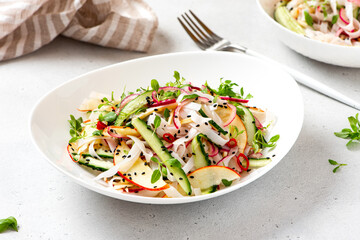 Rice noodle salad with cucumber, apple, onion, sesame seeds, and herbs in a white bowl on a light concrete background. Vegan salad Asian style. Vegetarian food. Vegetable salad with rice noodles
