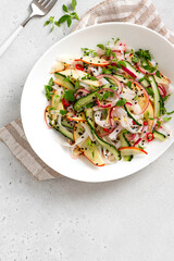 Rice noodle salad with cucumber, apple, onion, sesame seeds, and herbs in a white bowl on a light concrete background top view. Vegan salad Asian style. Vegetarian food.