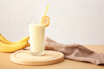 Glass of tasty banana milkshake on color table