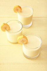 Glasses of tasty banana milkshake on color wooden background