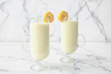 Cups of tasty banana milkshake on light background