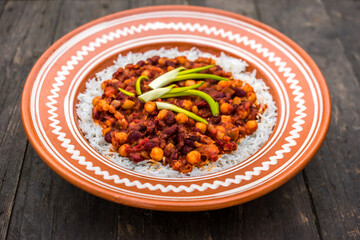Vegetarian red kidney beans chilli with chickpeas and tomato sauce in a traditional ceramic handcraft plate on a rustical wooden deck
