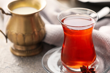 Glass of tasty Turkish tea and jug with milk on grey background