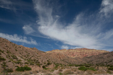 Desert landscape. View of the arid environment, sand, dunes and colorful mountains under a blue sky with beautiful clouds.