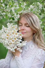 Fototapeta premium beautiful girl, a blonde in a vintage white dress walks in a blooming apple orchard, a bouquet of anemones, a bride